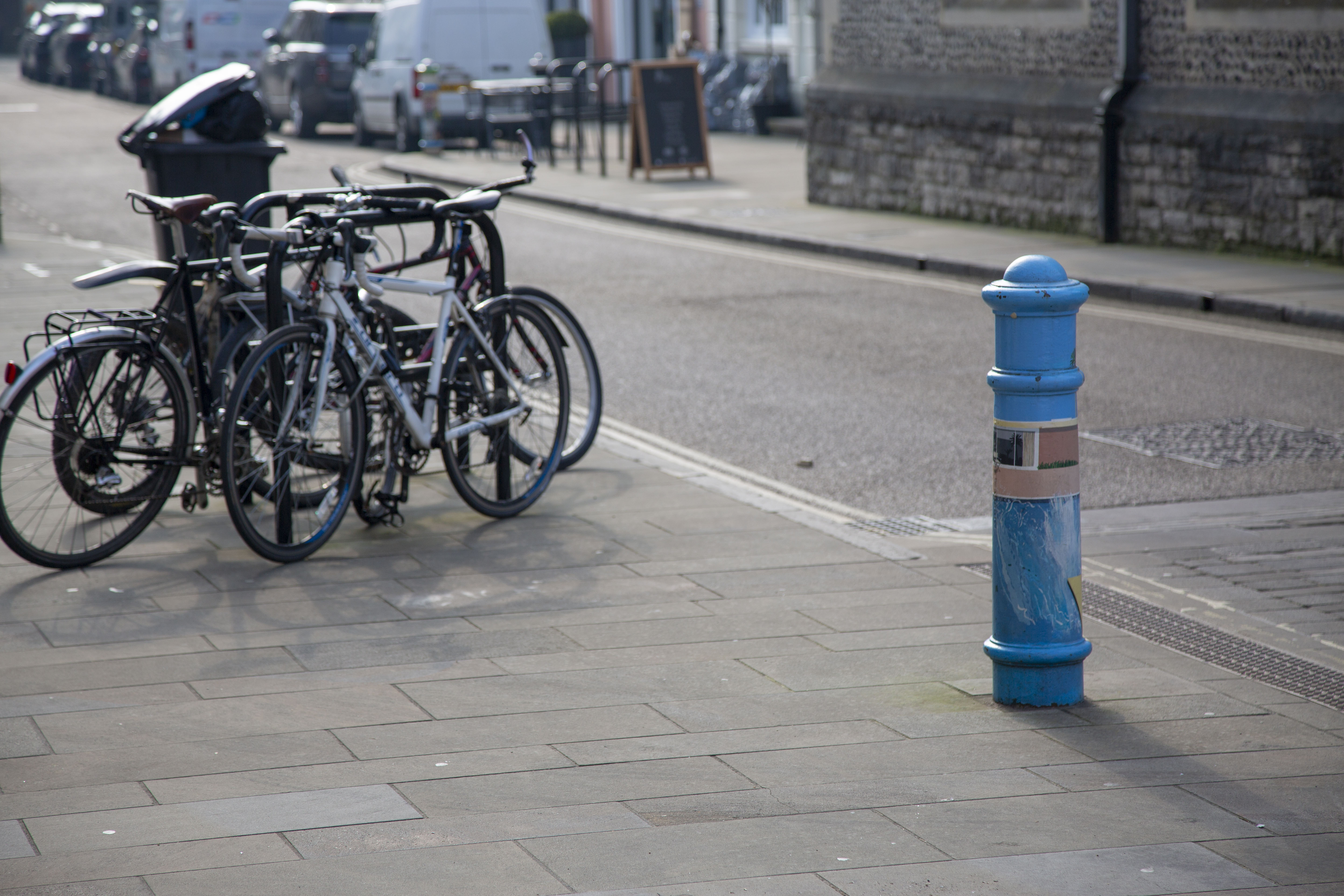A picture focusing on a bollard painted in the style of David Hockney's 'A Bigger Splash', with bikes in the background