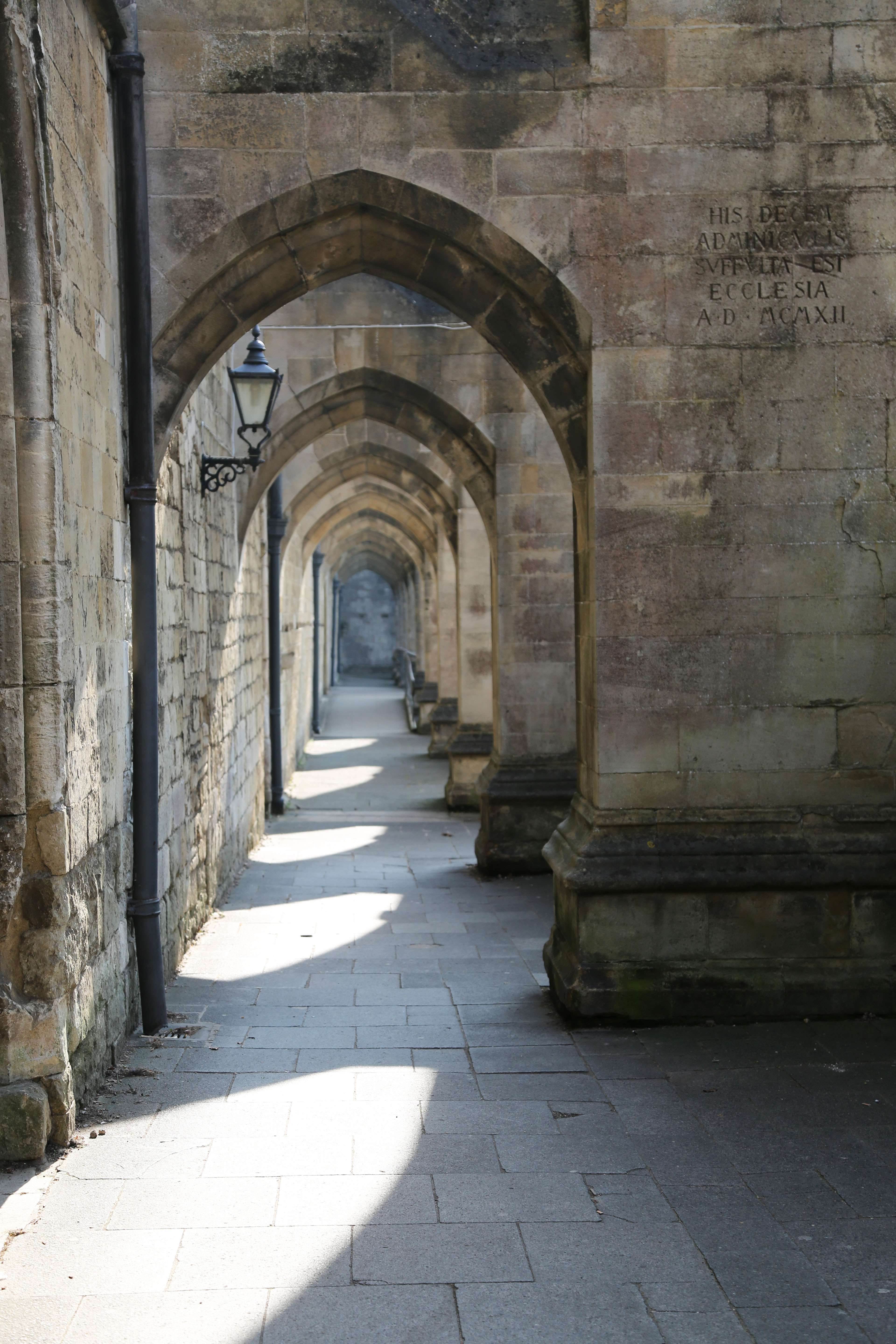 Arches cover a walkway that run adjacent to Winchester Cathedral, the sun causing shapes on the ground