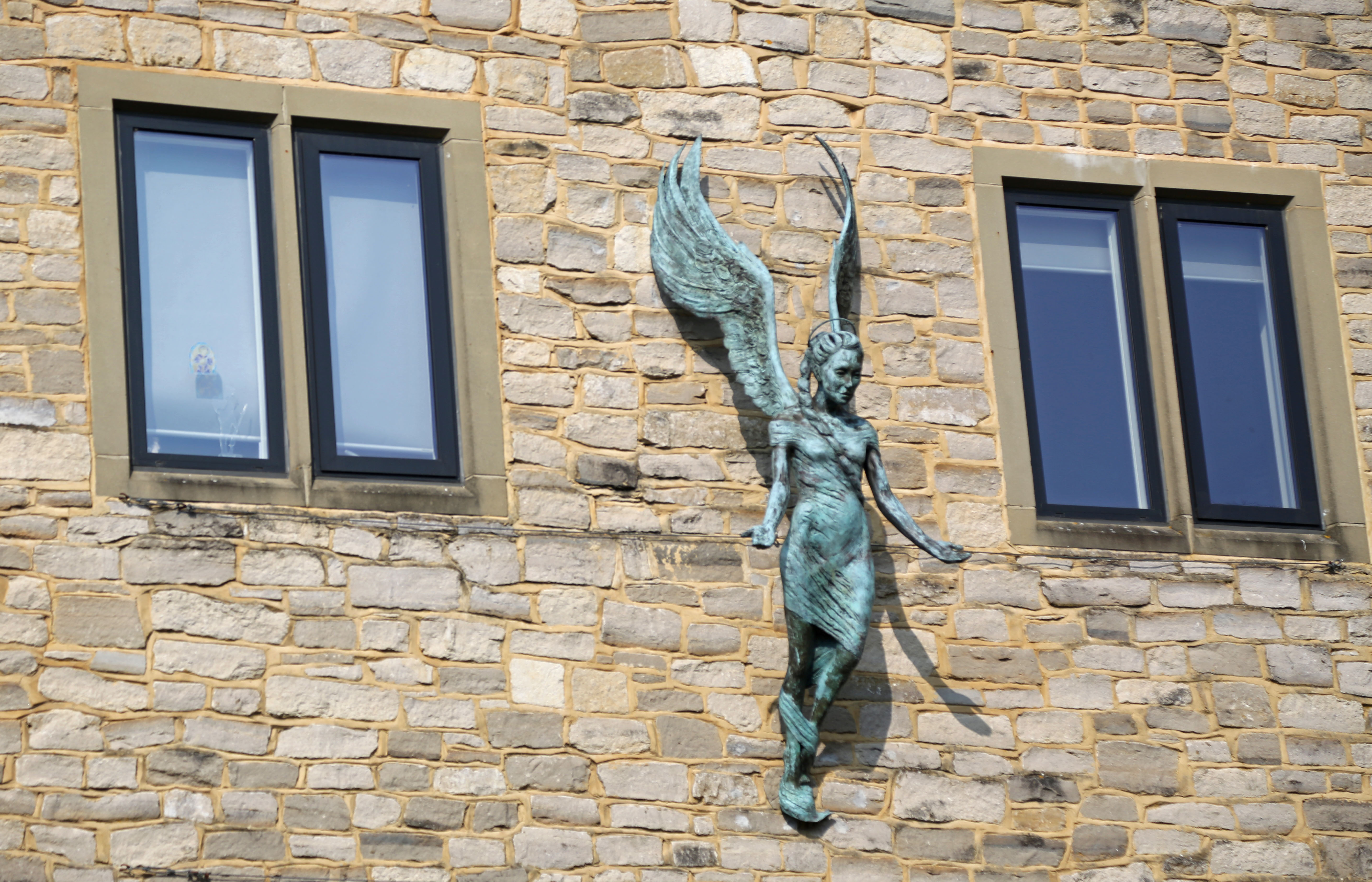 Statue of an angel in between two windows - the angel is blue and weather-warn