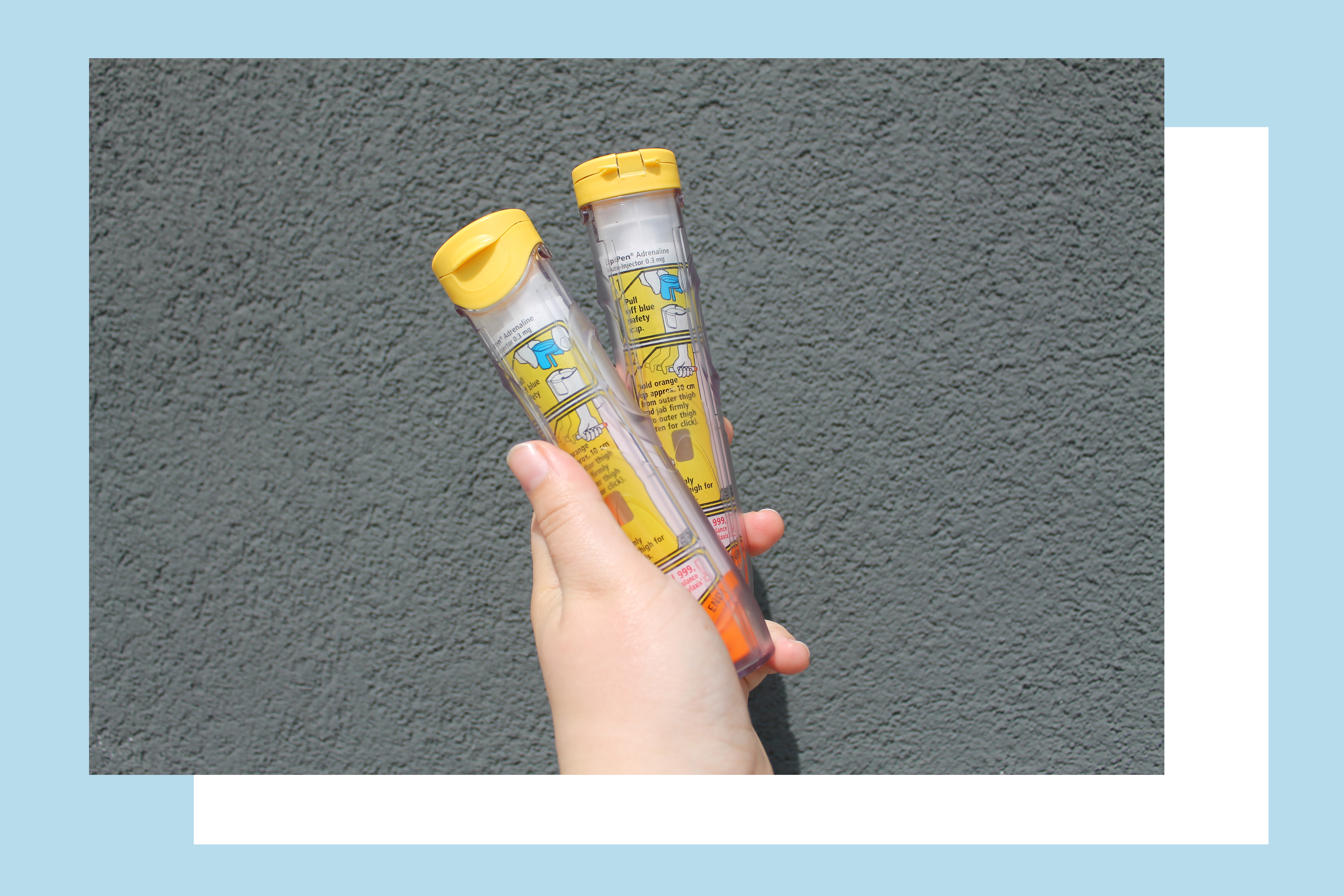 Rosie's hand holding two Epipens against a grey wall