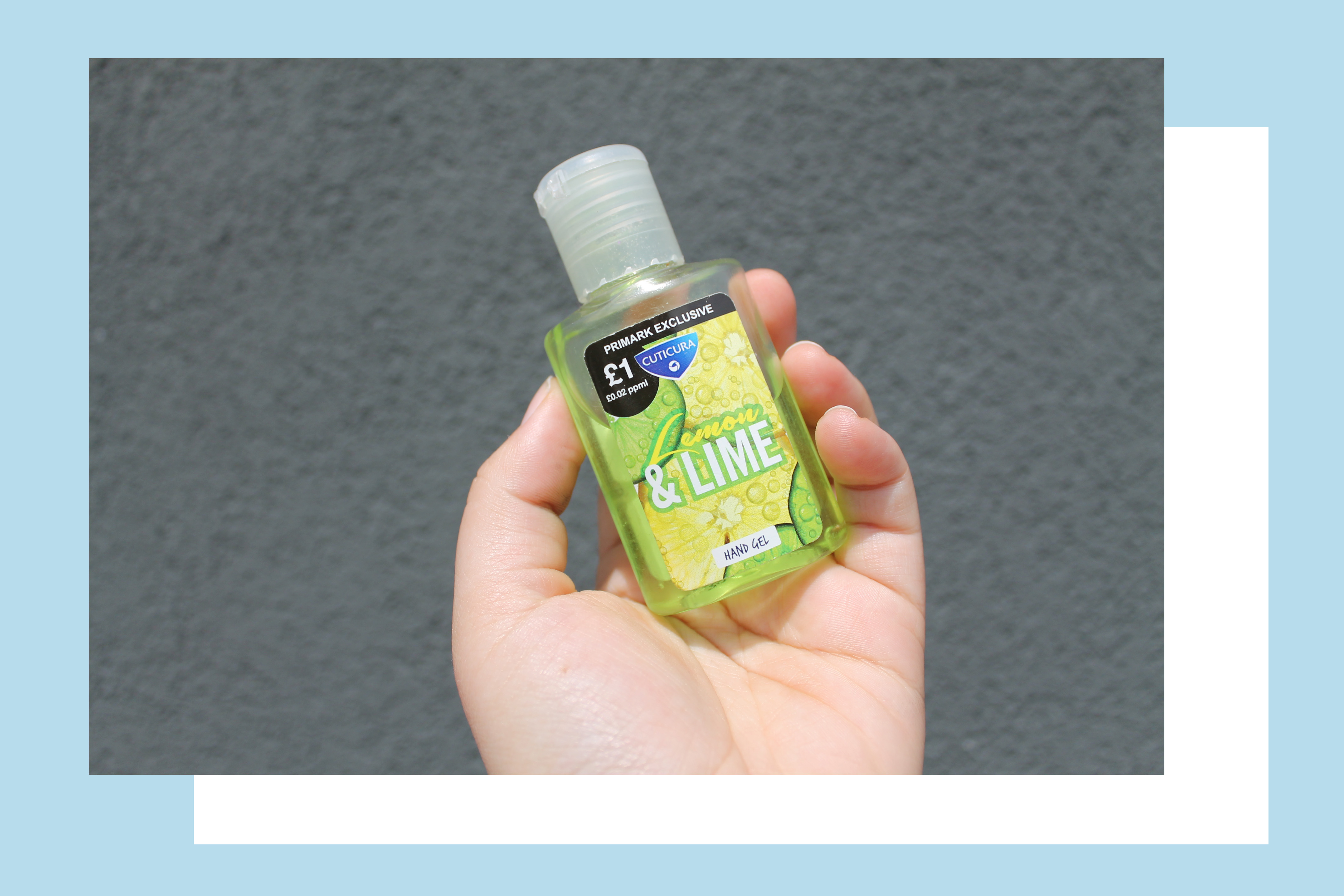 Rosie's hand holding a small bottle of green Lemon & Lime scented hand sanitiser, against a grey background