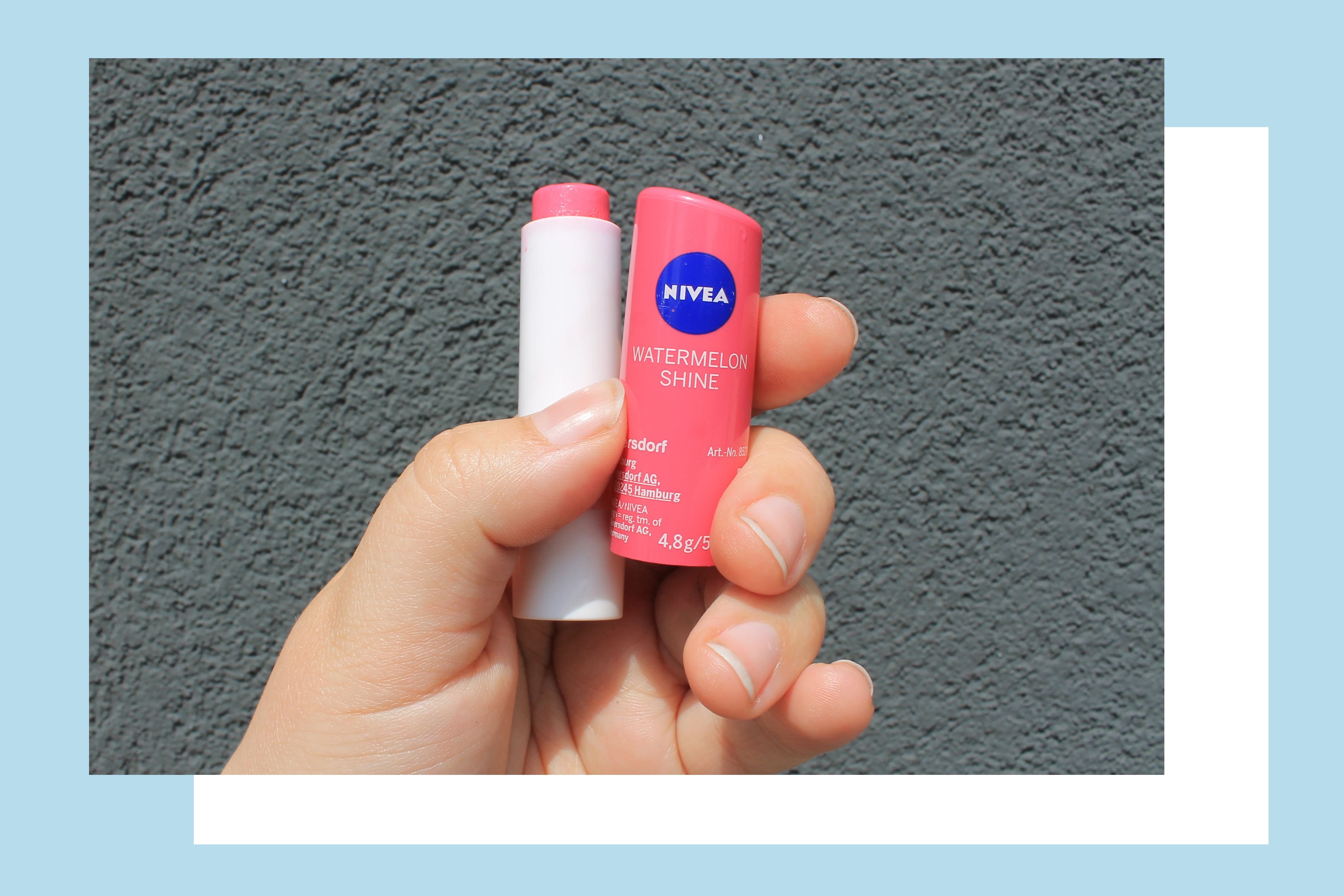Rosie's hand holding the pink packaging of Nivea's Watermelon Shine lipbalm against a grey background