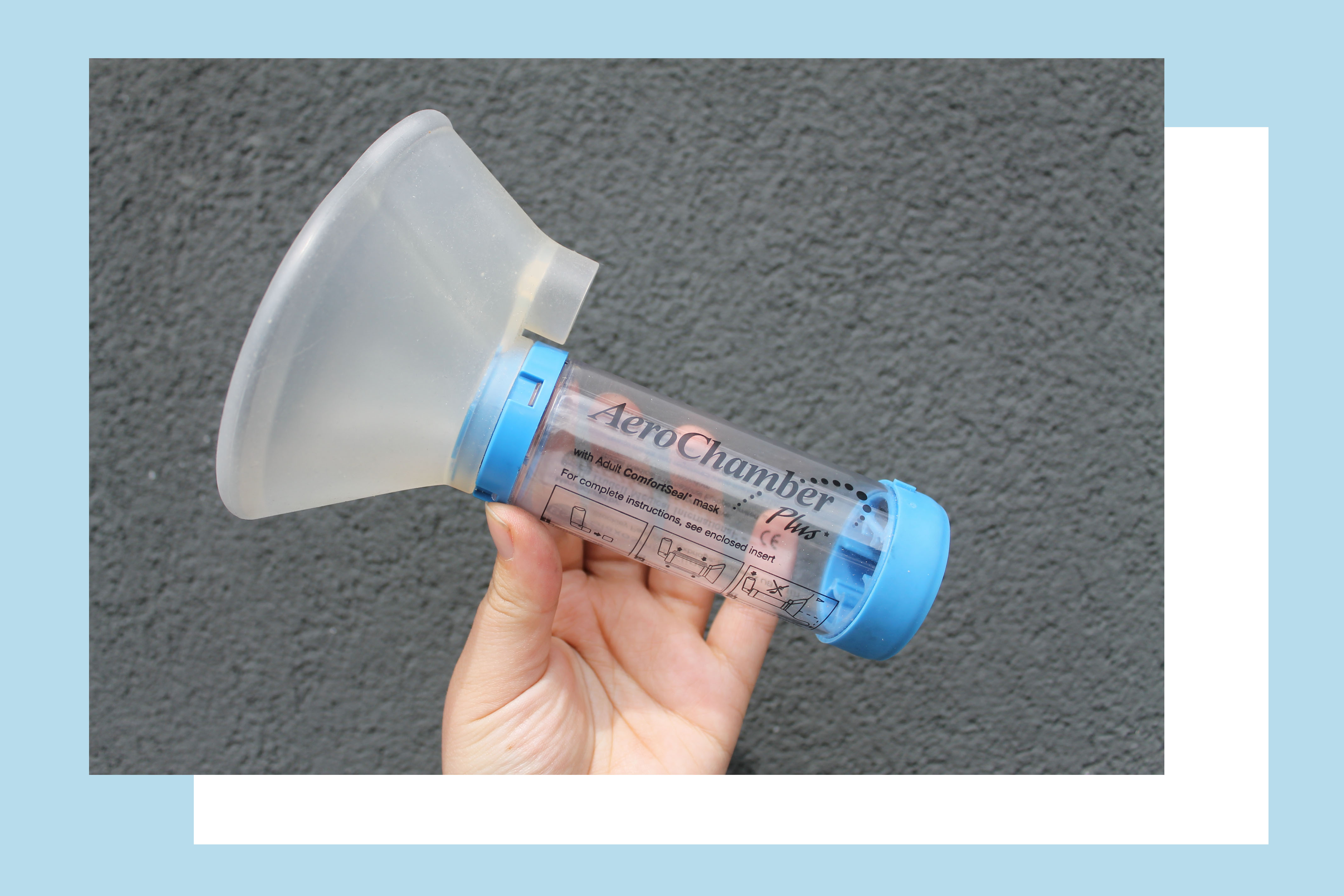 Rosie's hand holding an AeroChamber made up of a mask and a tube, against a grey background