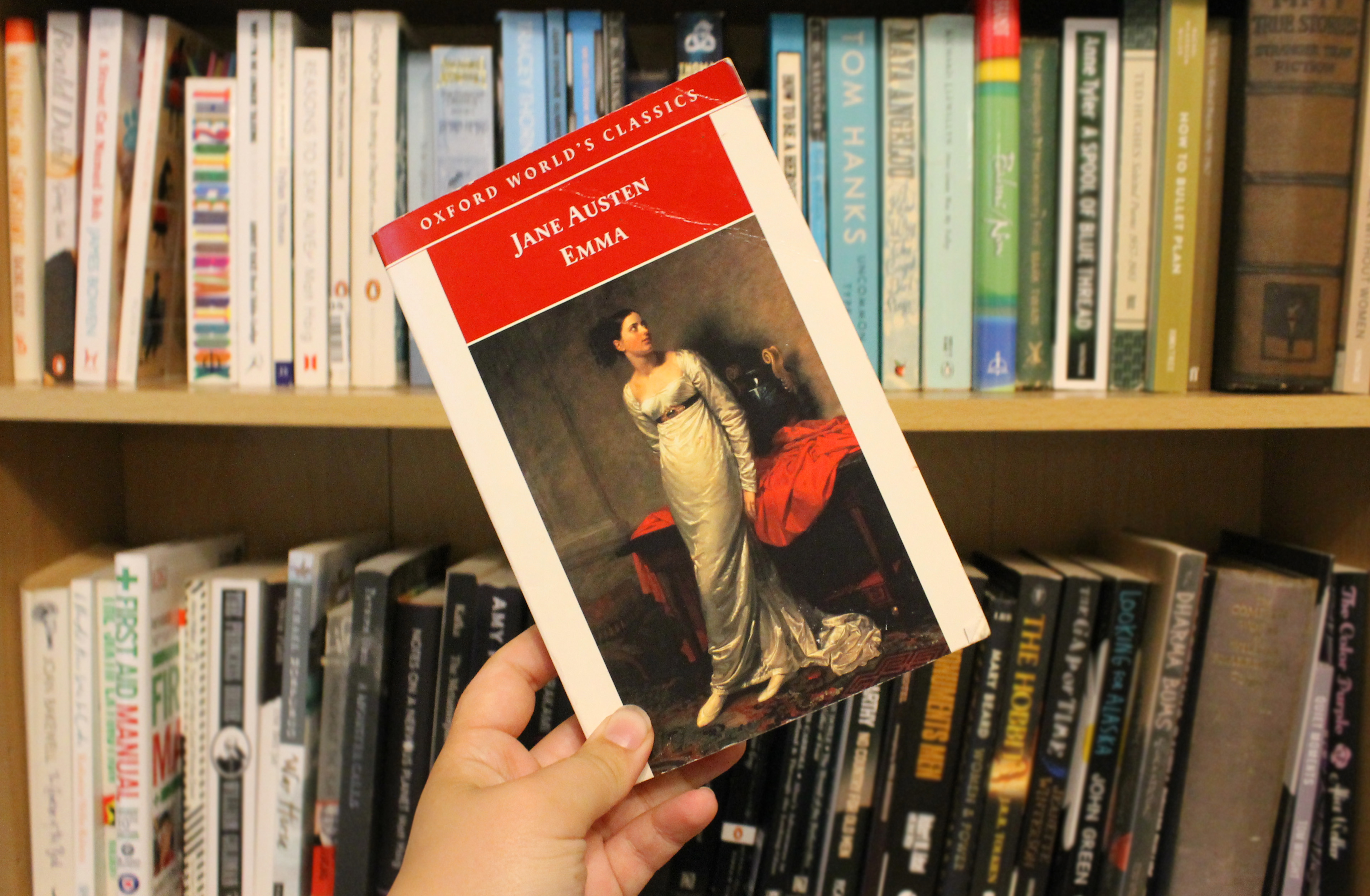Cover of Jane Austen's 'Emma' in front of a bookshelf. The cover shows a picture of a young woman looking in the distance