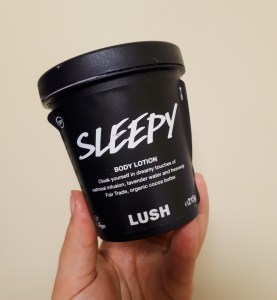 Rosie's hand holding a black pot of Lush's Sleepy