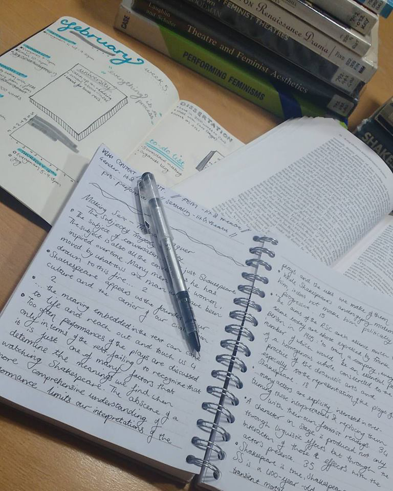 A bullet journal, academic text, and notebook lead out on a table