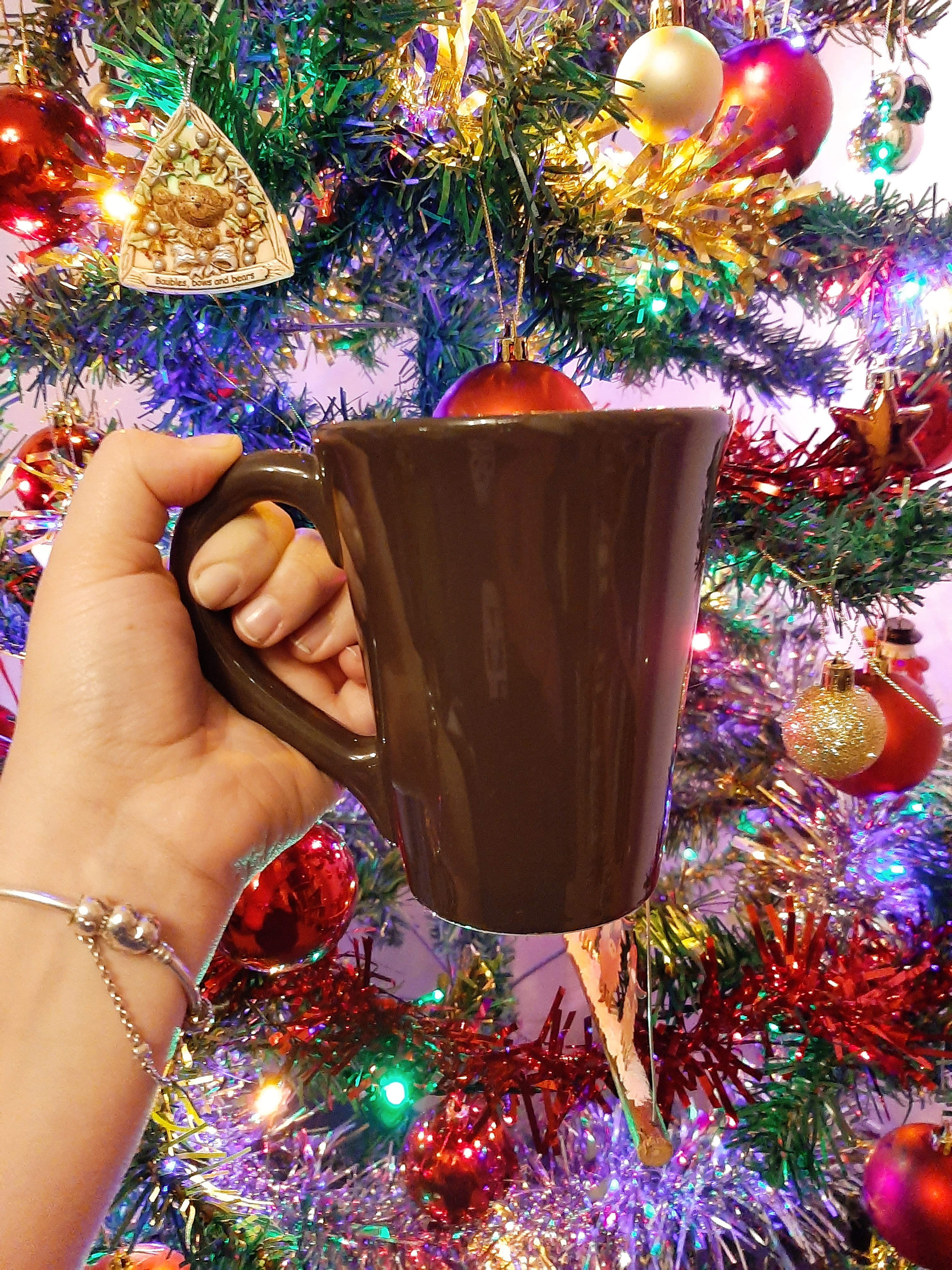 Rosie holding up her favourite mug against the backdrop of a lit Christmas tree