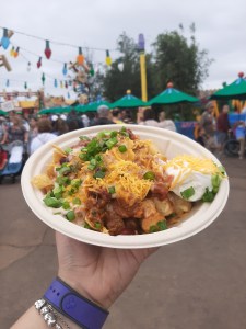 Rosie's hand holding up a bowl of totchos with Toy Story Land in the background
