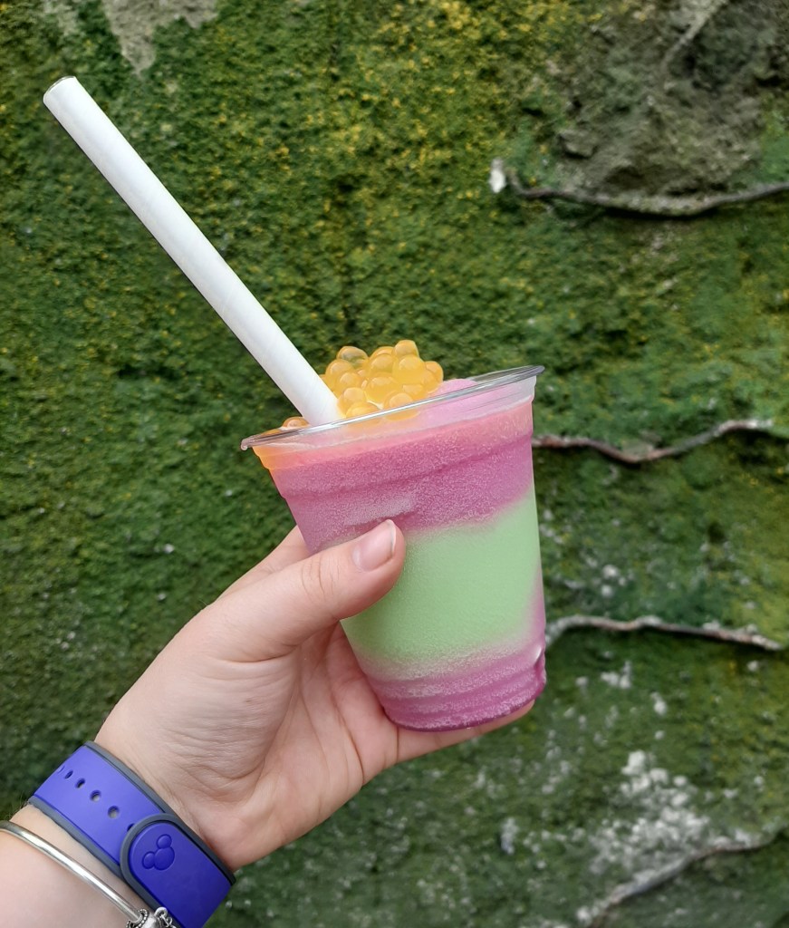A pink and green layer slushie drink topped with yellow boba balls