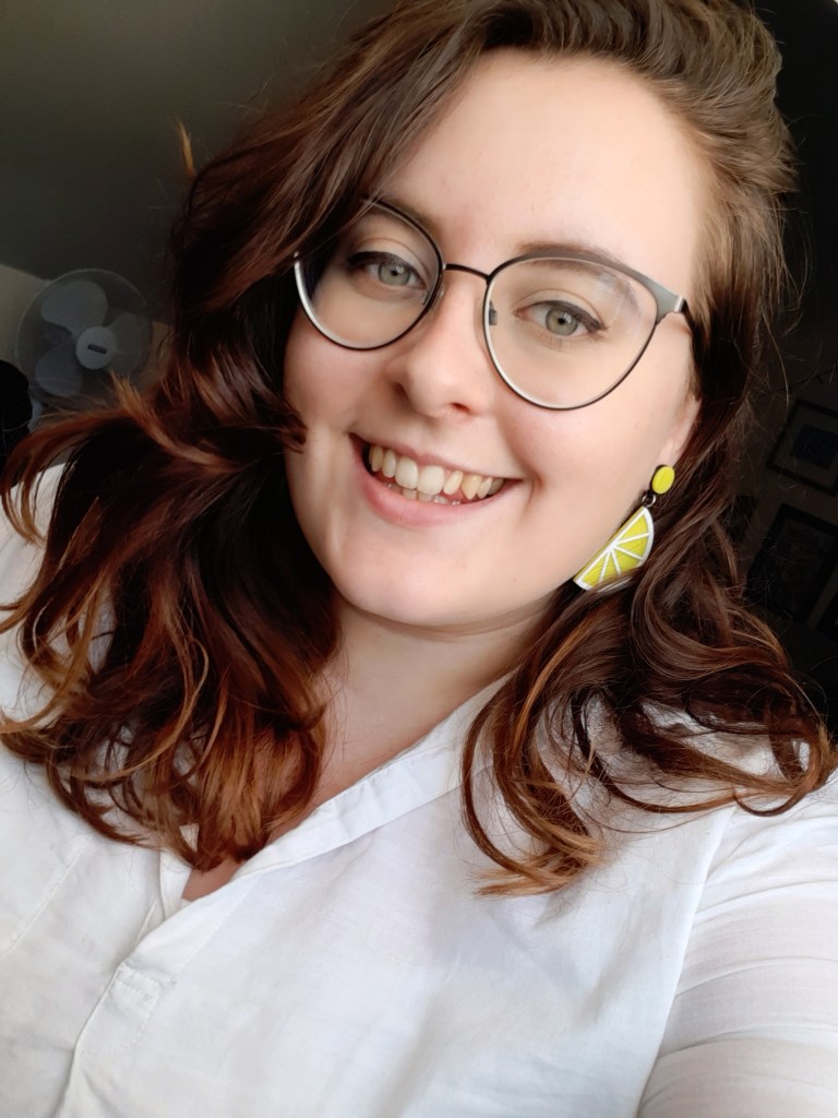 A picture of Rosie smiling. She is wearing a white blouse and yellow lemon earrings