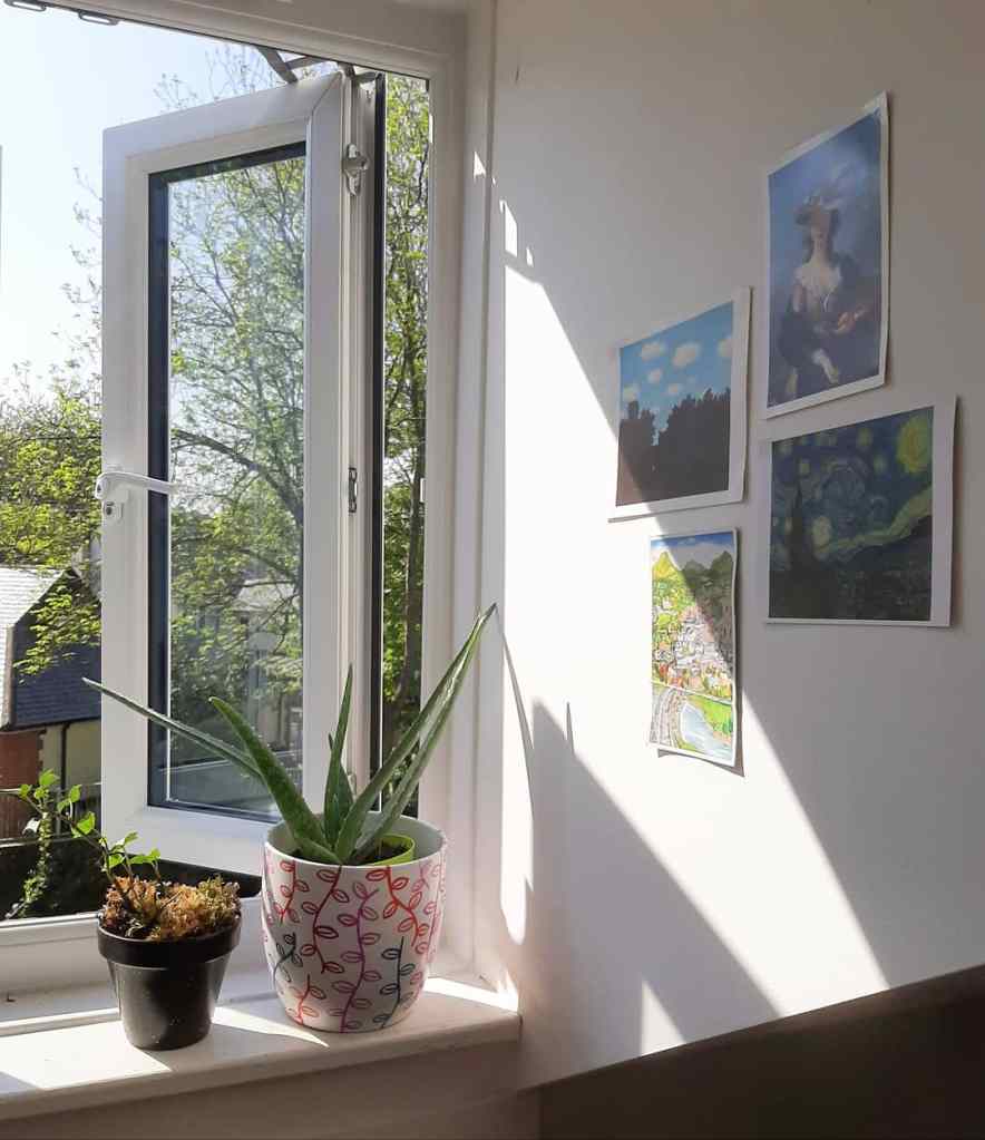 An open window with two plants on the sill. There are four pieces of art up on the wall