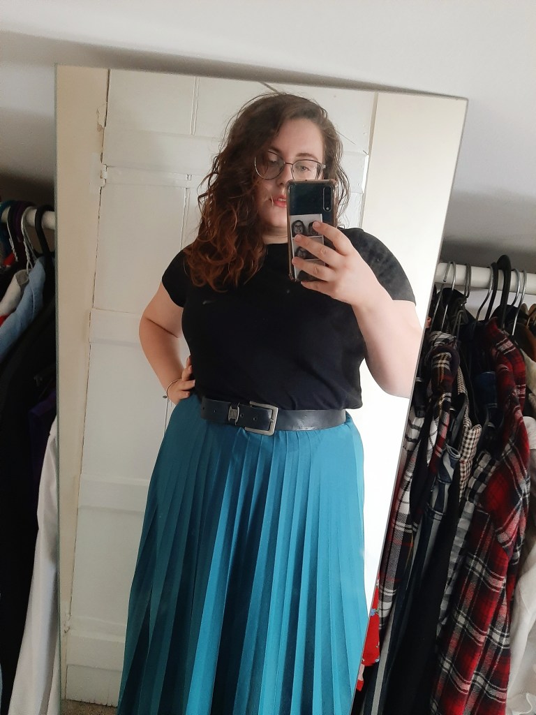 A mirror selfie by Rosie. She is wearing a blue midi skirt, with a thick black belt, and a black tee