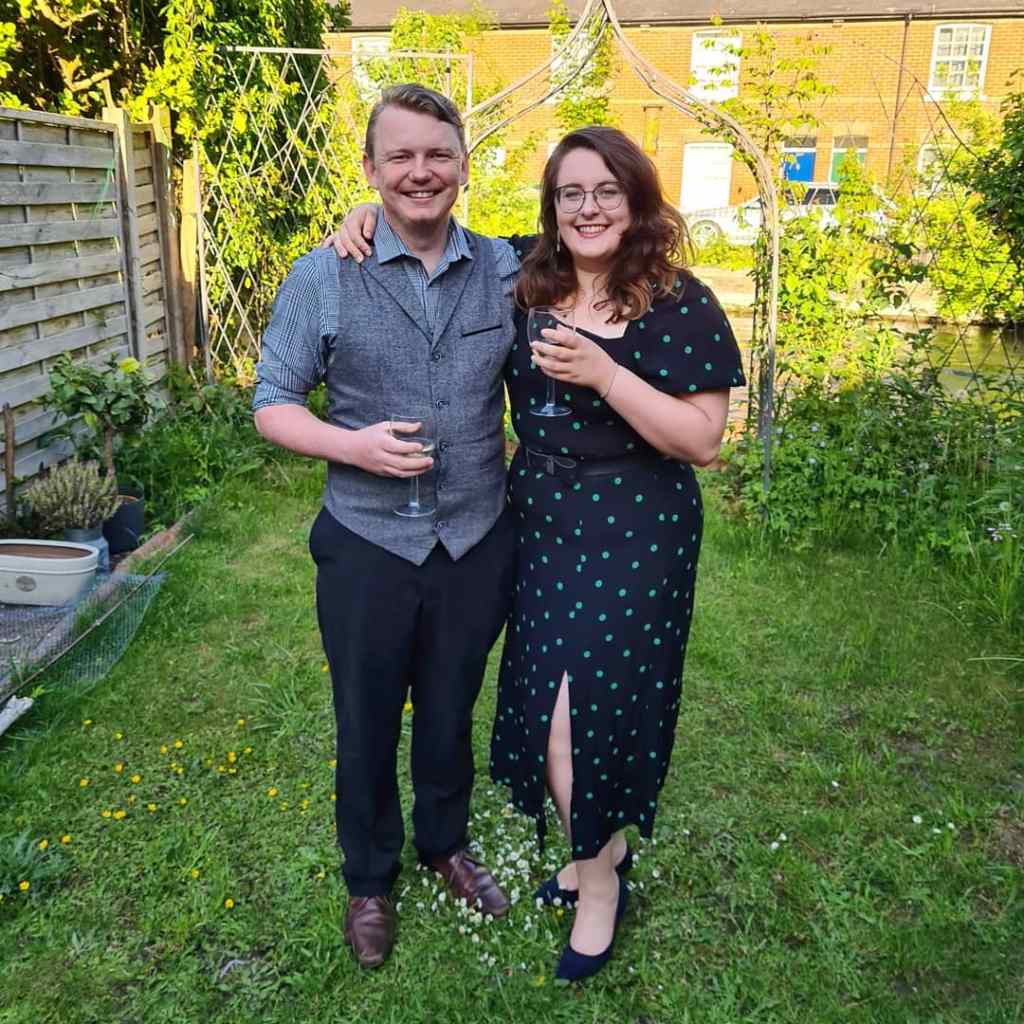 Rory and Rosie in their back garden, smiling. Rosie is wearing a black dress with green dots from New Look