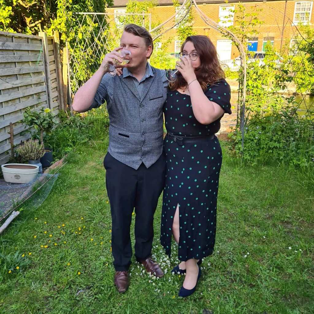 Rory and Rosie in their back garden, sipping wine. Rosie is wearing a black dress with green dots from New Look