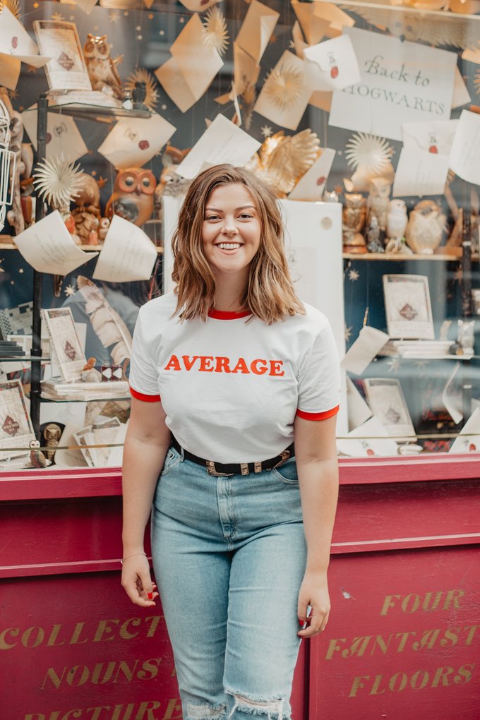 Lucy wearing pale blue mom jeans and a white tee emblazoned with the word 'AVERAGE' in red