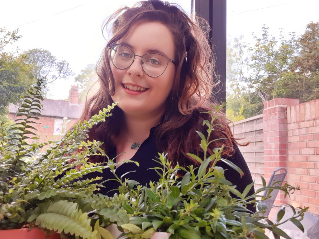 Rosie looking at the camera, with a slight smile. Two green plants are at the forefront of the image.