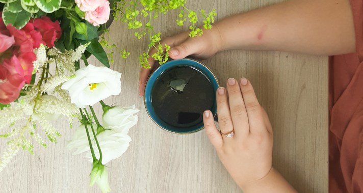 Flaylay of Rosie's hand around a blue mug, whilst she wears her engagement ring. There are pink and white flowers on the left.