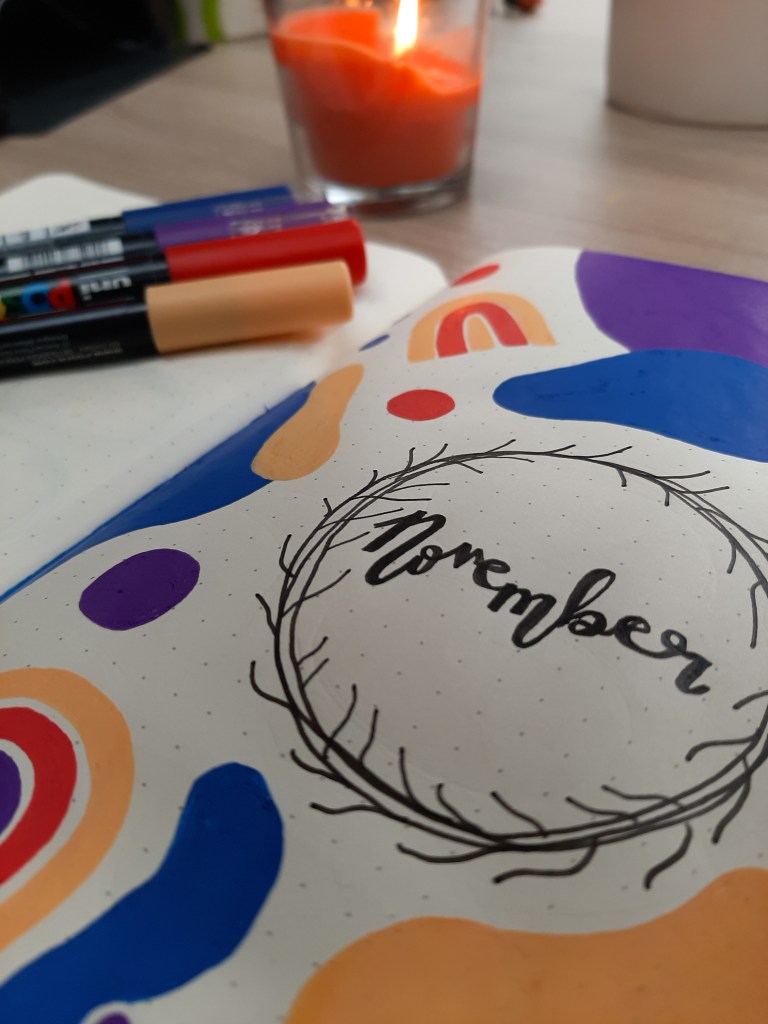 "November" written in calligraphy, surorunded by primary colour doodles. Four Posca pens are in the background.