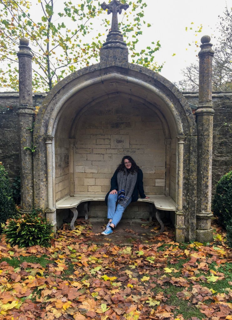 Rosie is sat in on a grey stone bench, surrounded by yellow leaves