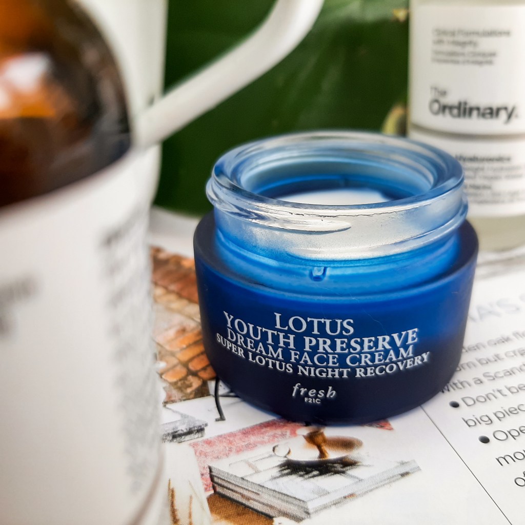 A blue tub of Fresh's Lotus Youth Preserve Dream Face Cream. It is on a white and black background.
