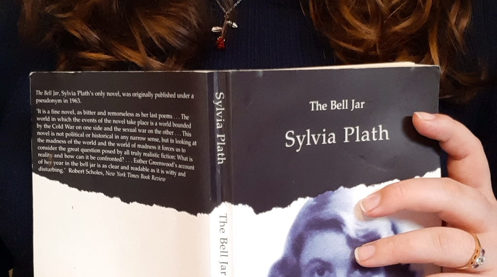 A white and black cover of Sylvia Plath's The Bell Jar. Rosie is holding it with her left hand.