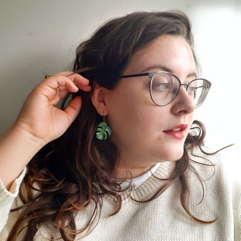 Rosie looking to the right. She has brown hair, is caucasian, and is wearing glasses. She also has green monstera earrings.
