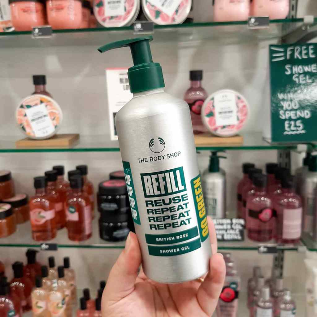 A silver bottle, with green decal, including the words 'refill' and 'The Body Shop'. The background is made up of pink skincare products.
