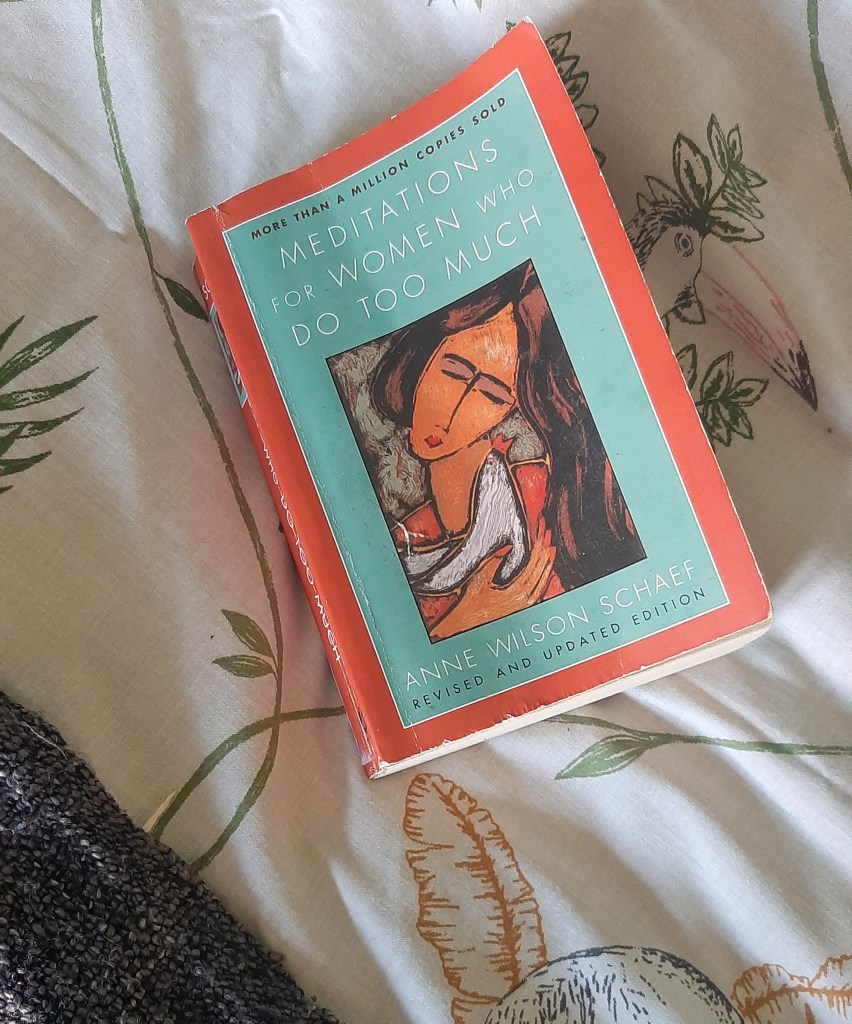 A book with a blue and read cover, with a drawing of a brunette woman on a cover. It is resting on a white and green cover with drawings of animals.