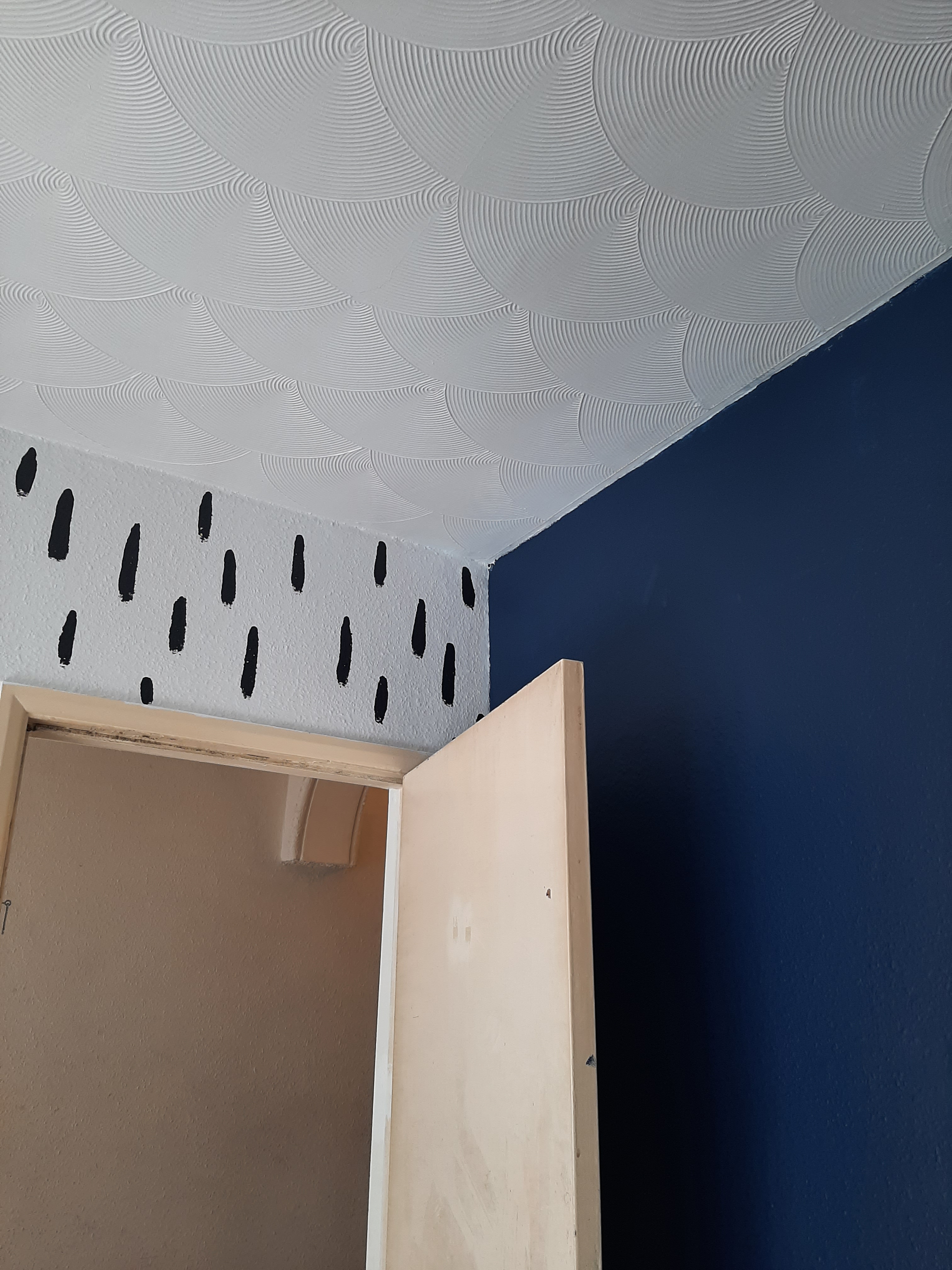 An image of the freshly painted lounge. One wlal is white with black lines, one wall is deep blue, the ceiling is white, and the door is an unpainted, dirty yellow.