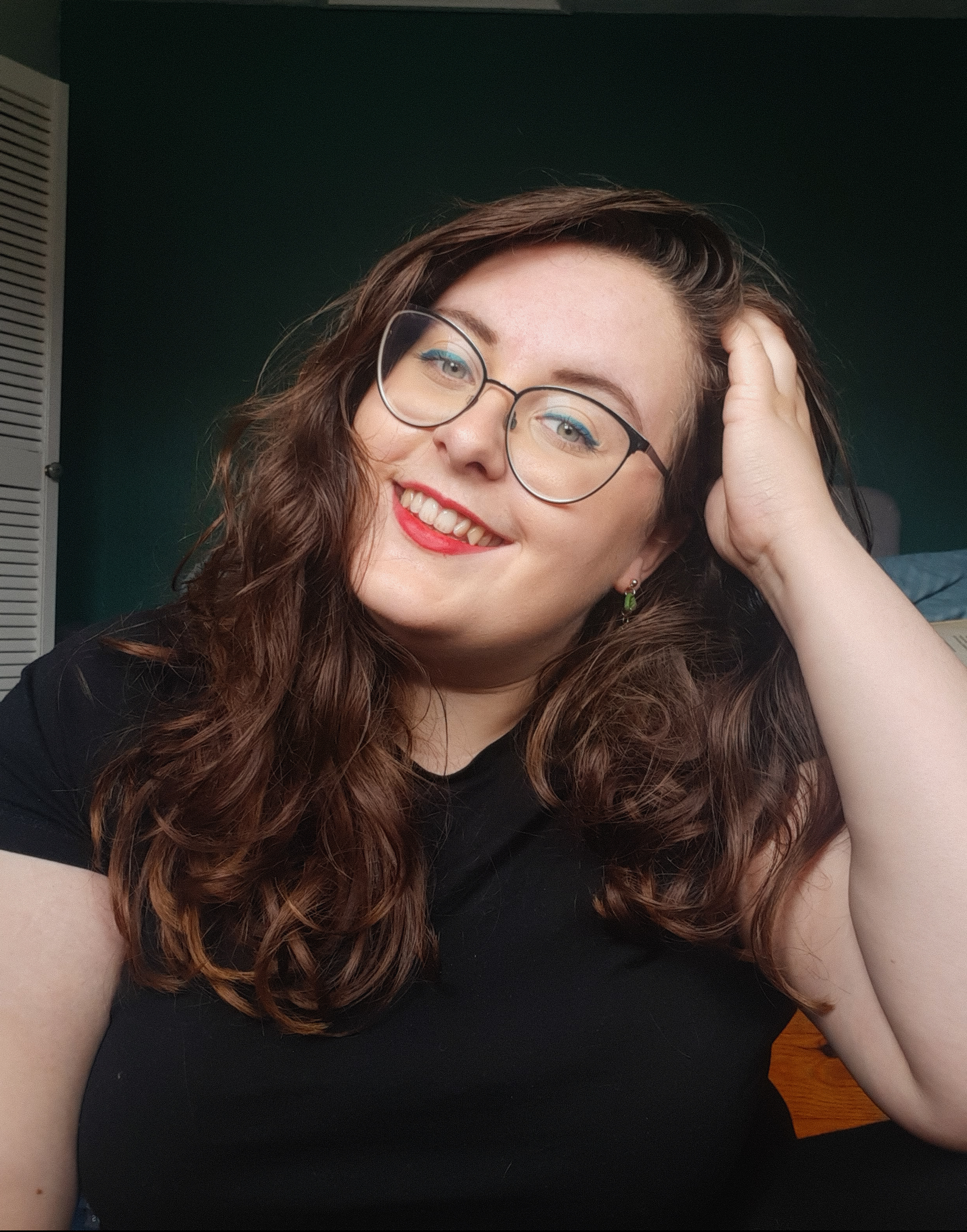 Rosie looking straight at the camera. She has a hand in her hair, wear lips, glasses, and a blue cat eye liner