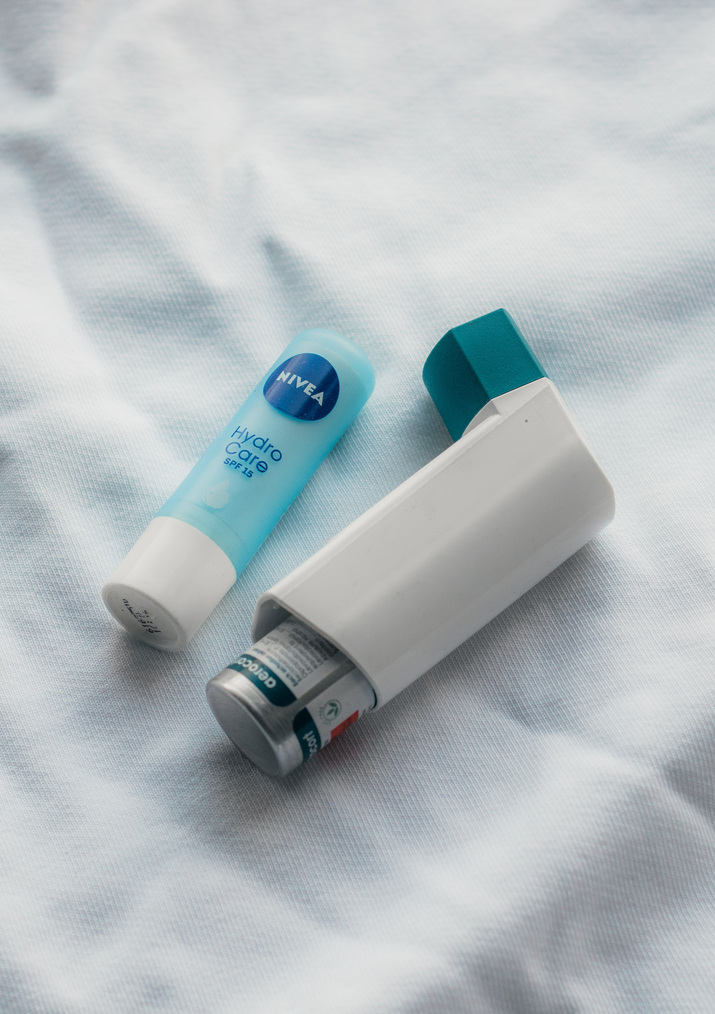An image of a white and blue inhaler and blue chapstick on a white cloth background.