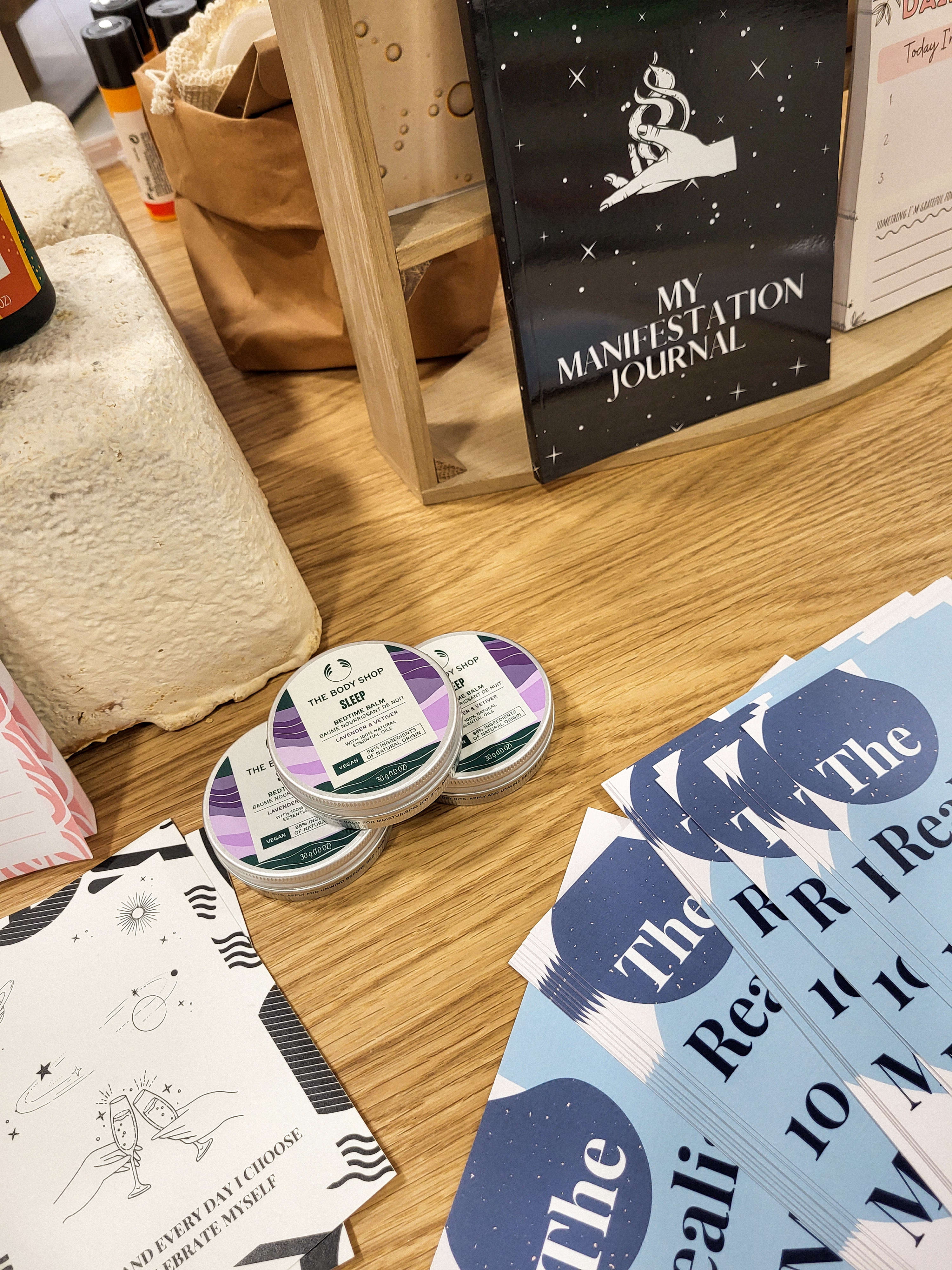 Purple tins surrounded by white paper affirmation cards, a black pile of paper, and a black journal that says "my manifestaion