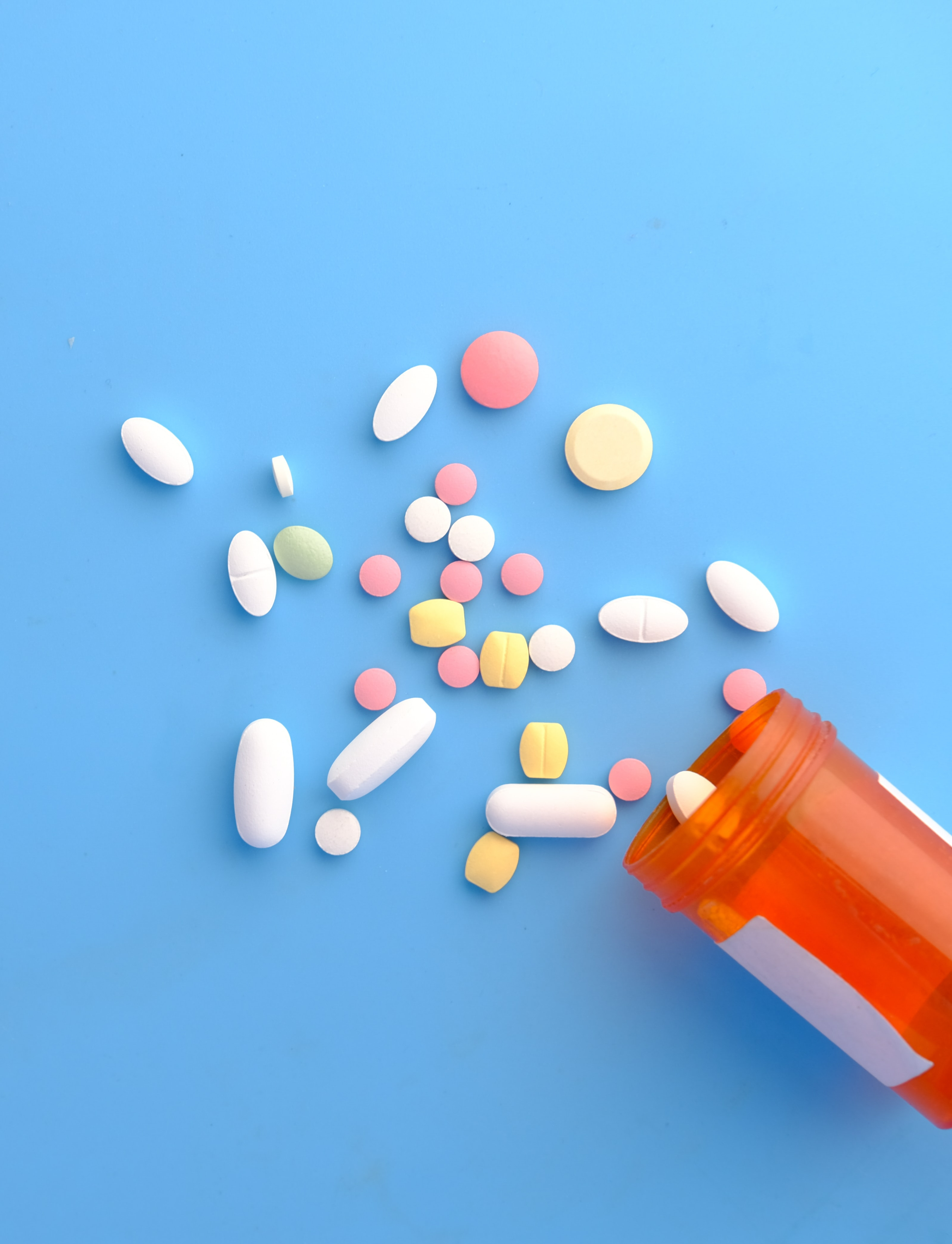 An orange pill tub, with pills spilling out onto a blue background.
