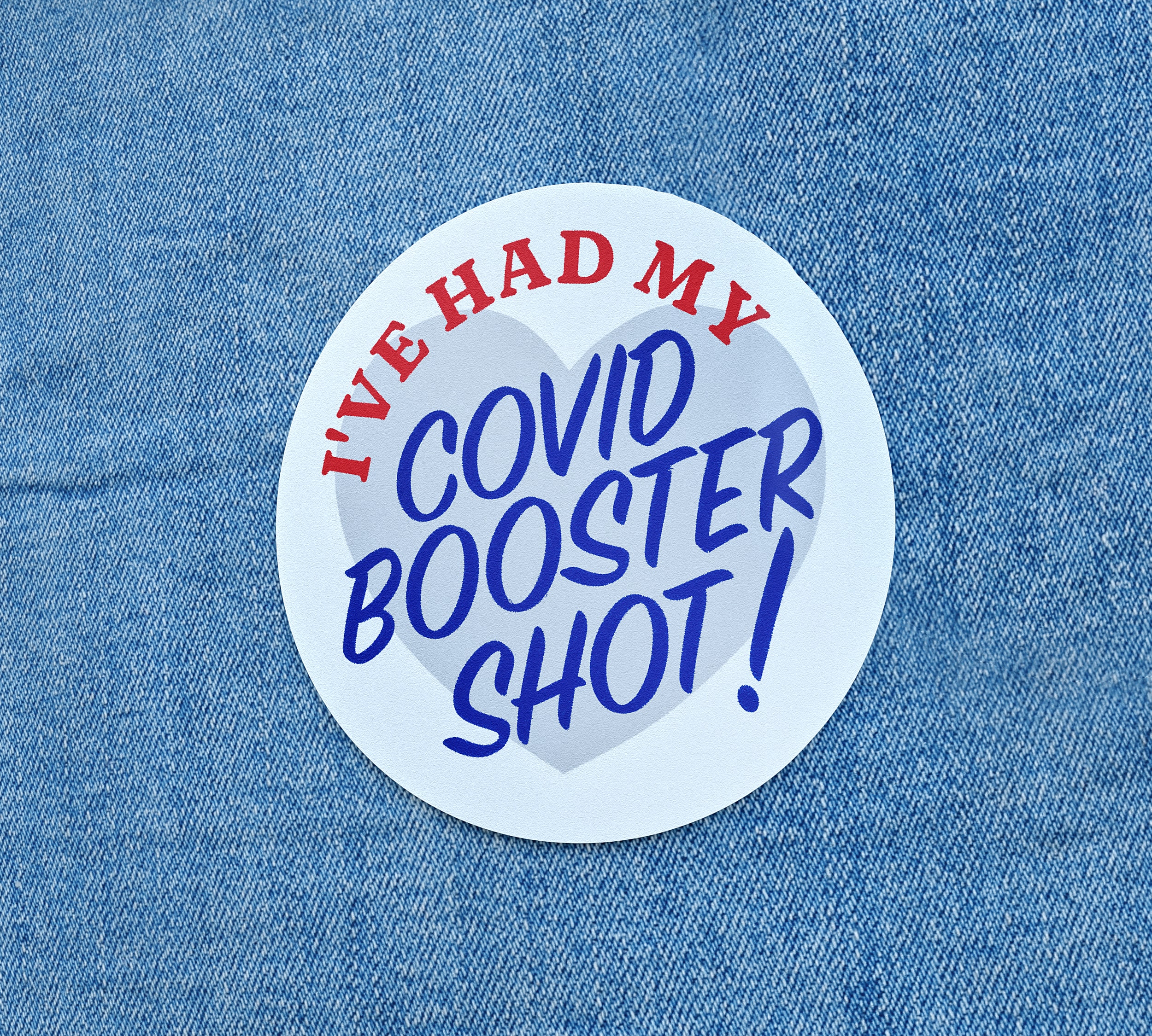 A blue denim background with a white circulr sticker that says 'I've had my covid booster shot!' in red and blue.