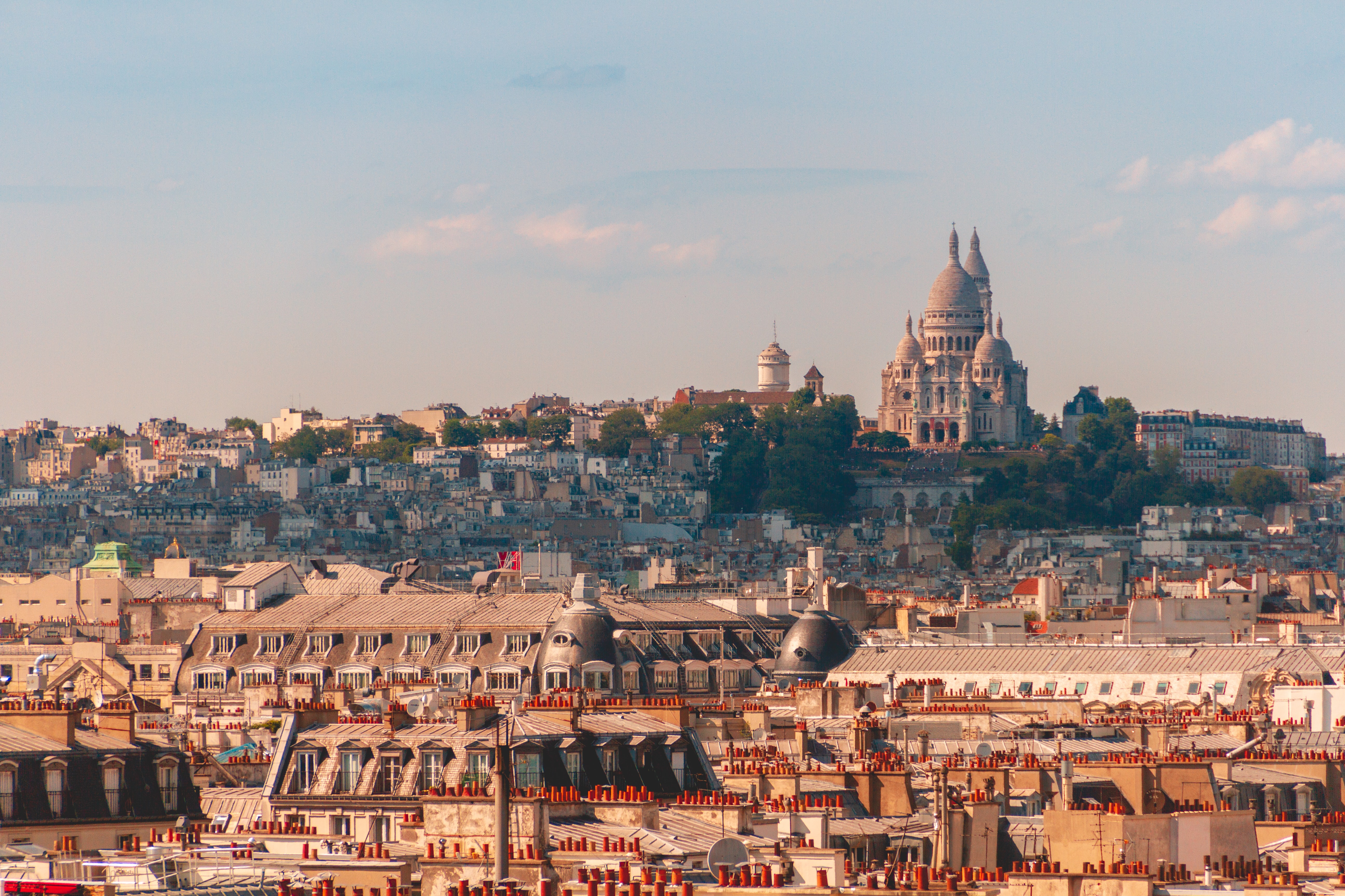 The view of Paris on a hill. The sky is blue. Under it, sits a white historical buildings