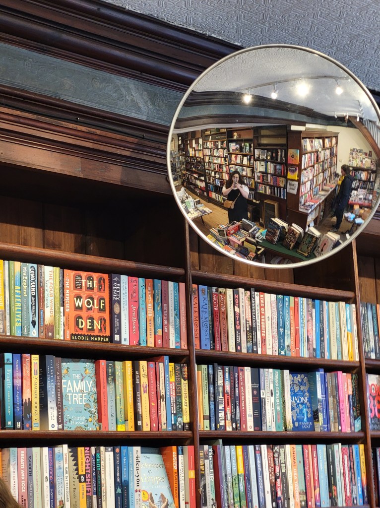 AN image of Rosie in a circular mirror. The mirror is on a bookshelf full of books