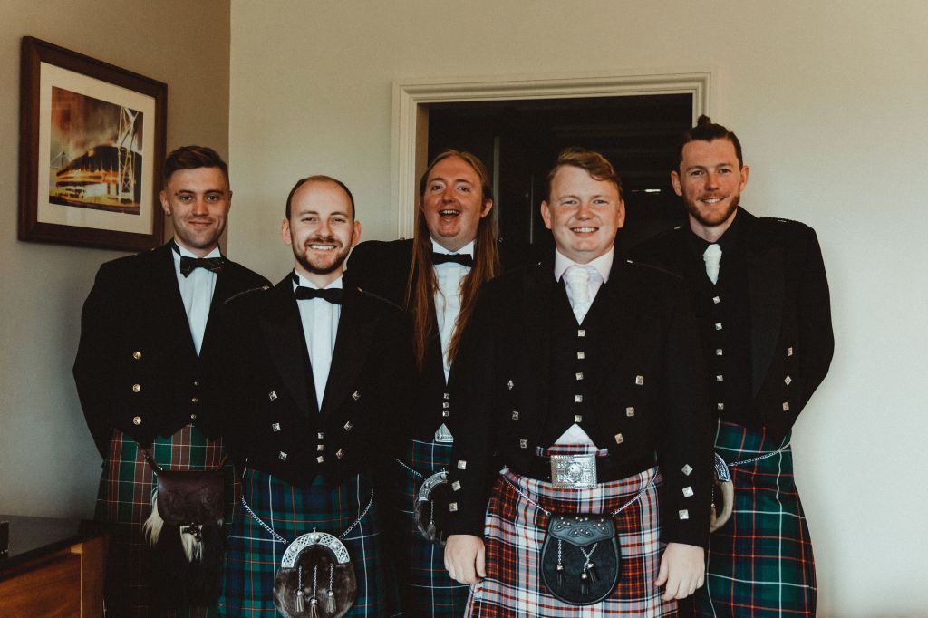 The group of groomsmen at the Blincow wedding. There are five white men in a row, all in shorts, ties or bowties, tartan kilts, and with sporrans. They are all looking at the camera.