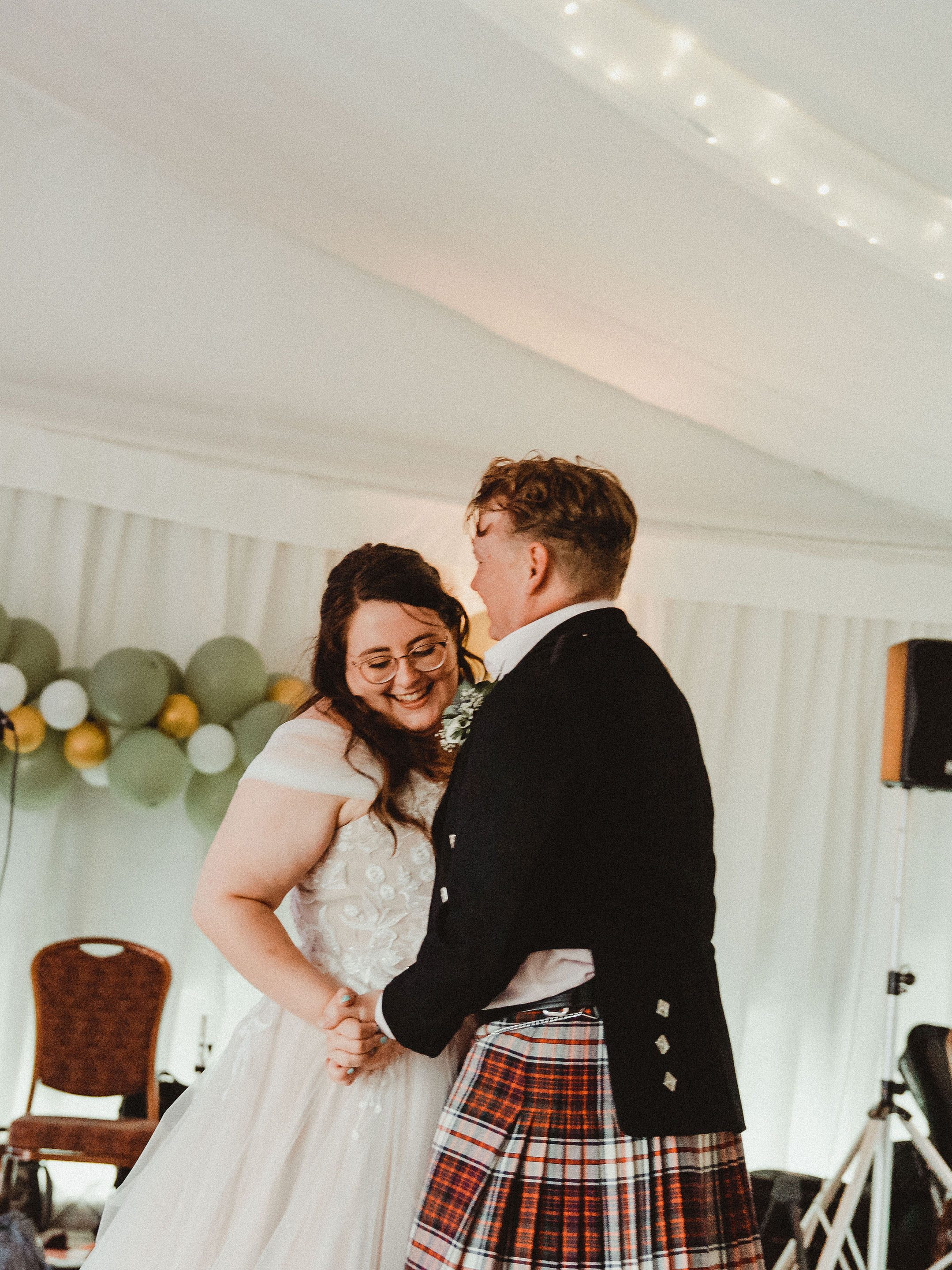Rosie and Rory's first dance. Rosie is  on the left in a wedding dress and is smiling whilst looking down. Rory is to the right.