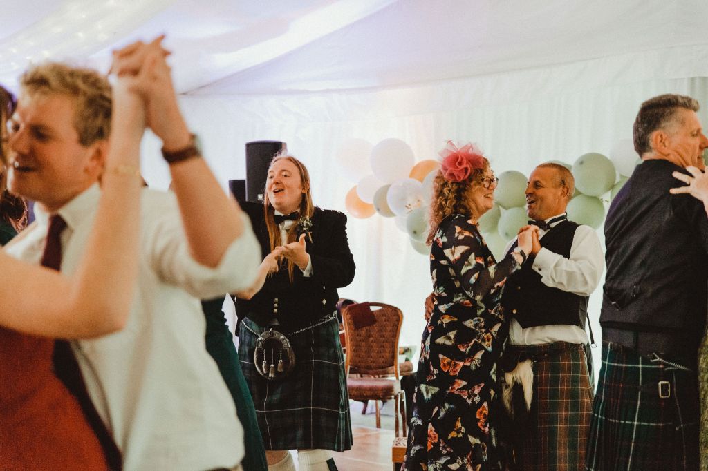 A group of people dancing at a wedding. There is one person in the middle applauding. 