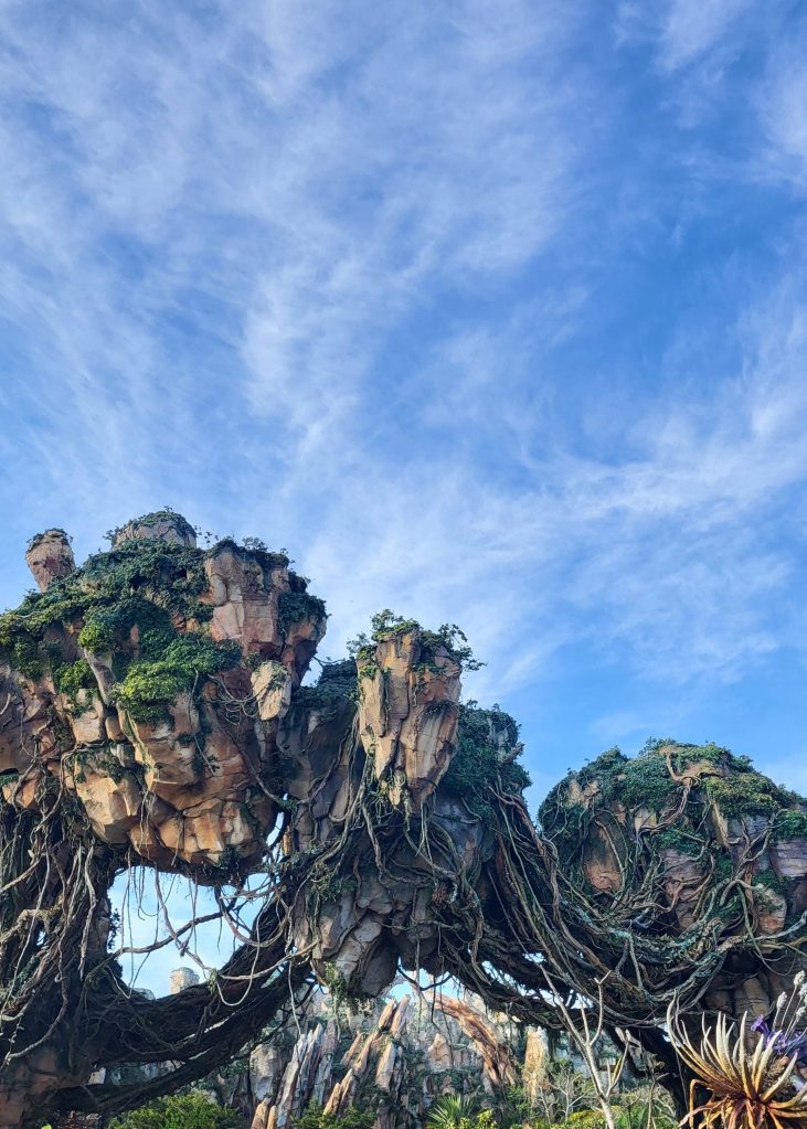 An image of clumps of rocks seemingly floating in the air. They are covered with vines and greenery. Above the rocks are a blue and white sky. 