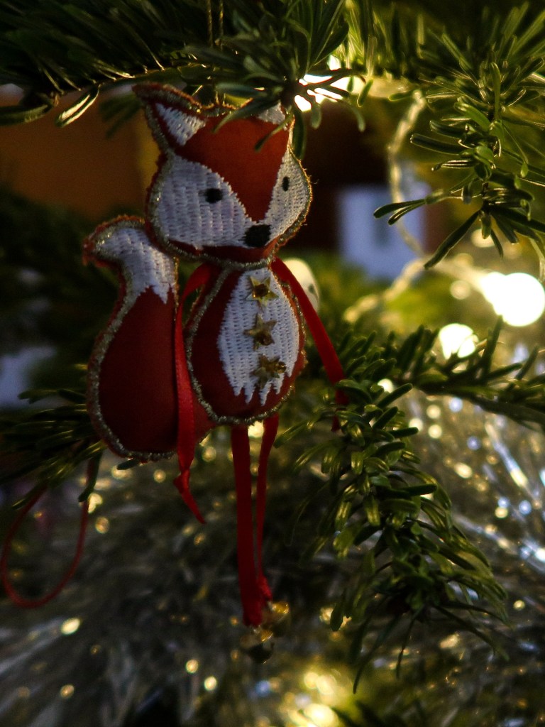 An image of a knitted fox ornament of the branches of a Christmas tree.