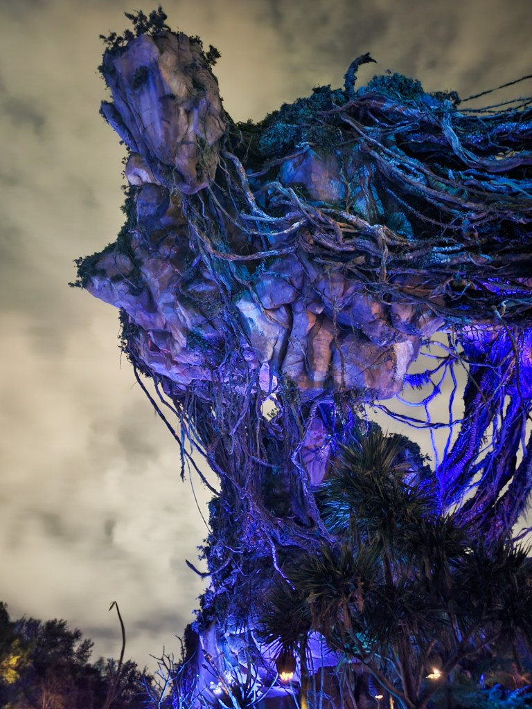 floating mountain at pandora An image of the floating mountains at Pandora. It is one rock covered in vines and plants, lit up in purple. The sky is grey behind it.