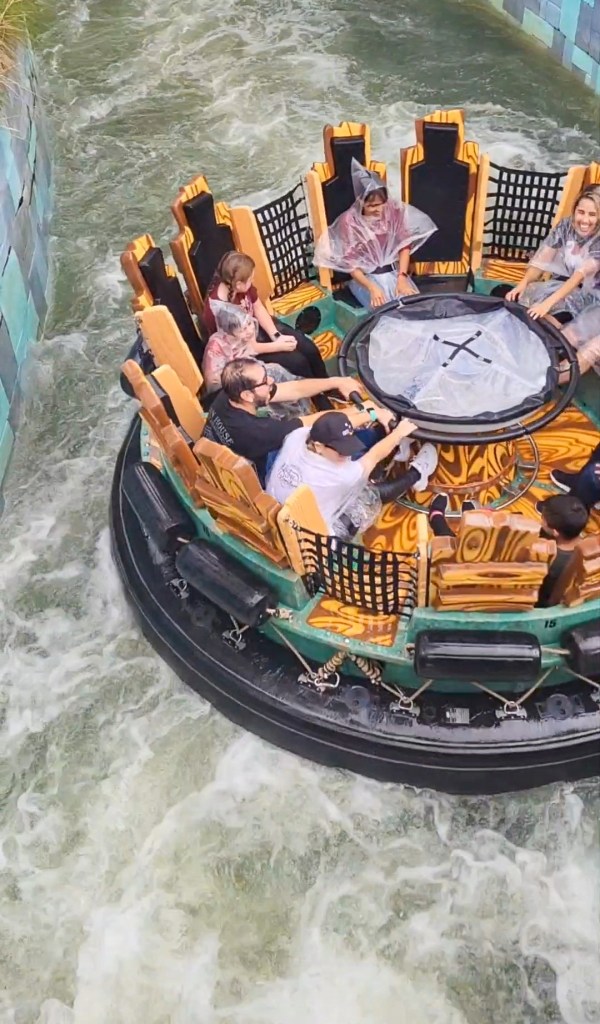 universal water ride An image of a round raft vehicle on a man-made river. The water is white and bouncing. There are people in the raft sat in a circle. They are all wearing clear or white ponchos.