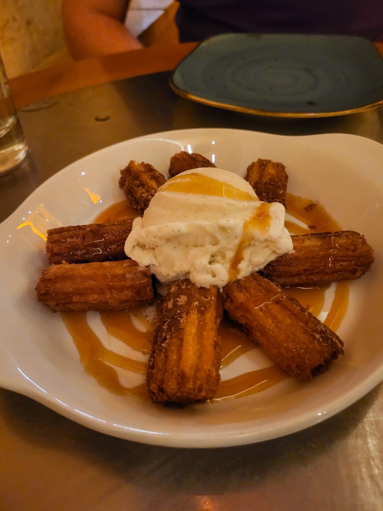 Churros and vanilla ice cream covered in caramel in a white bowl. 