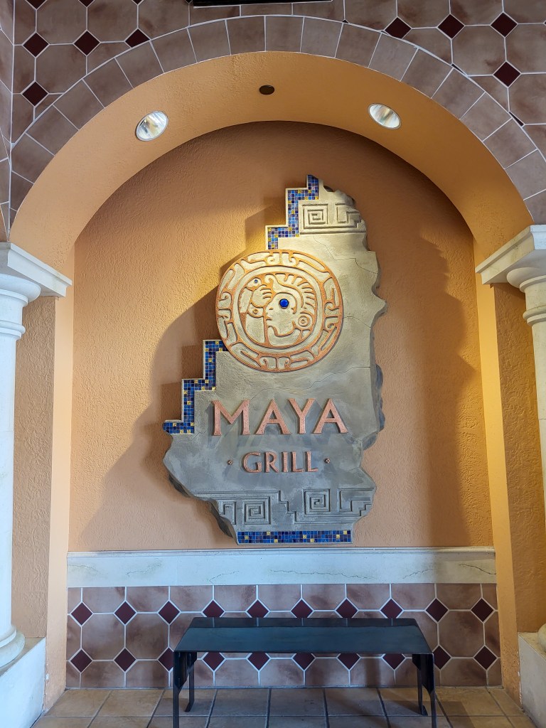 An orange arch way drawing focus to a grey sign that says 'Maya Grill' in orange, with an orange emblem above.