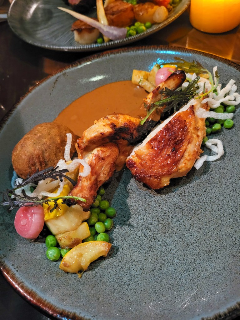 A blue plate topped with chicken breast, peas, croquettes, white crisps, and an orange sauce.