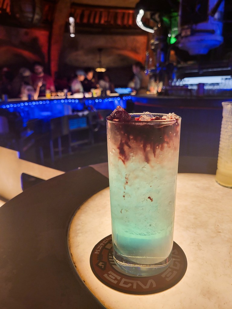 A tall blue drink with red syrup on top, sat on the bar