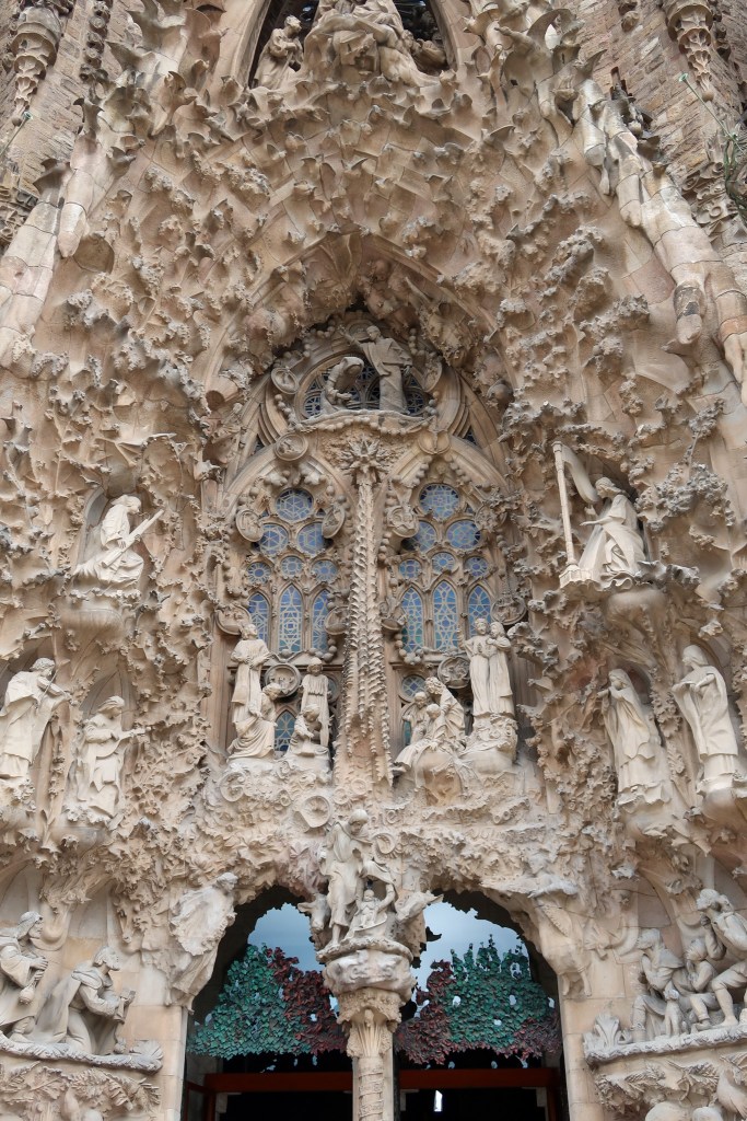 The carved, grey stone entrance to La Sagrada Familia. There are some glass windows featured but mainly there are numerous carvings, mixtures of people and wildlife. 