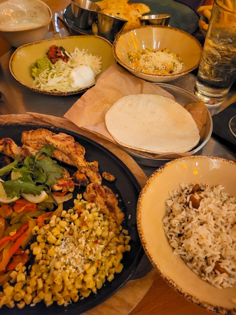 Bowls of Mexican food, including corn, wraps, rice, and guacamole