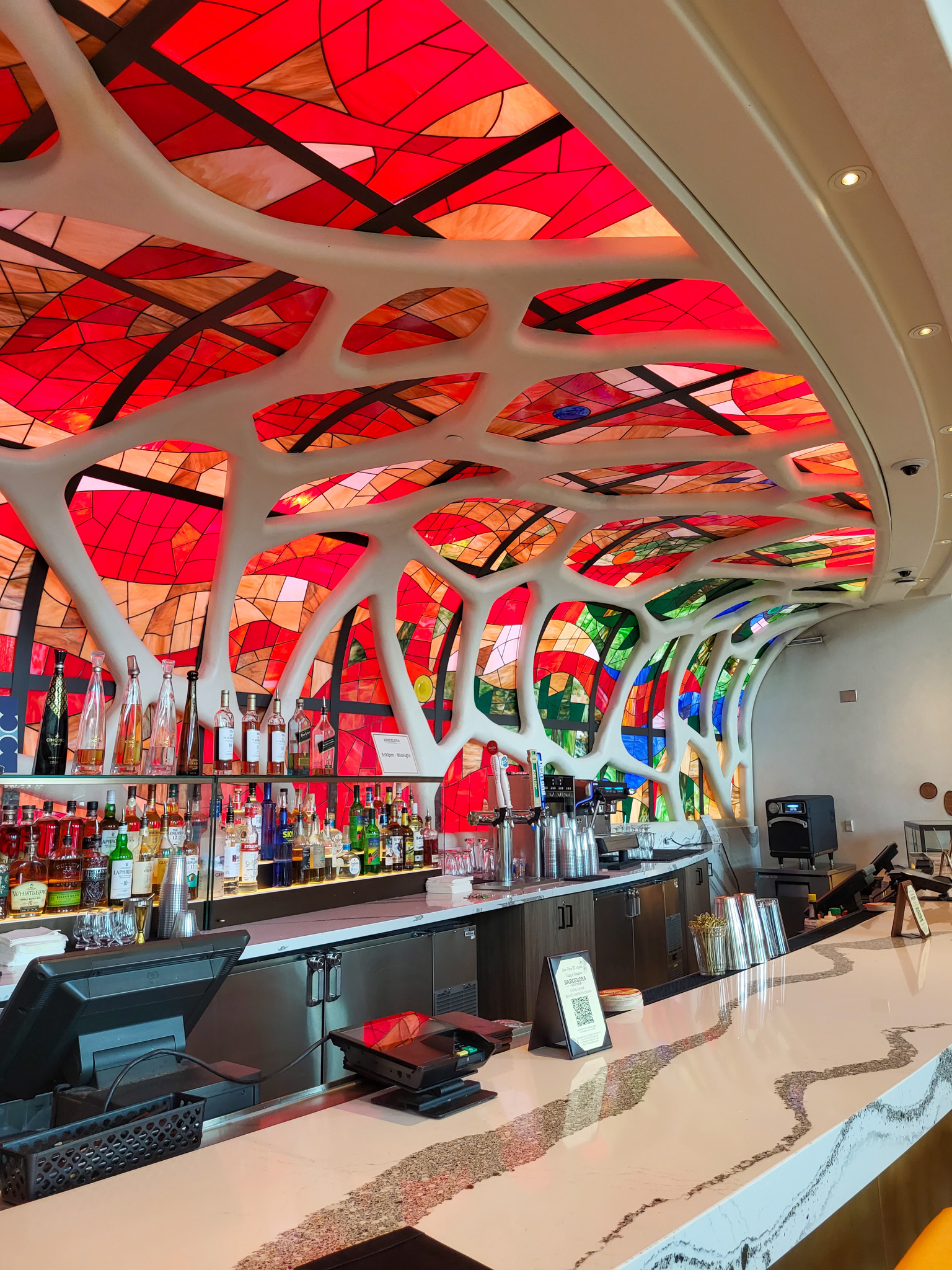 An alcoholic bar with a red stained glass as a backdrop.